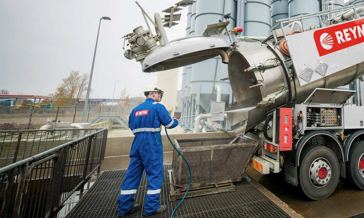 REYM-medewerker in blauwe overall reinigt met een hogedrukspuit een container bij een REYM-vacuümwagen